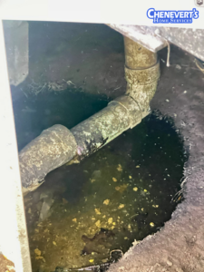 A corroded pipe joint is surrounded by standing water in a dirt crawl space. Chenevert's Home Services logo is visible in the top right corner.