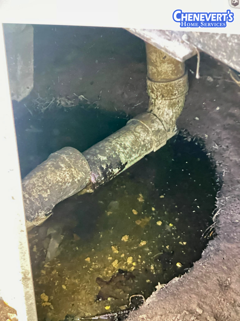 A corroded pipe joint is surrounded by standing water in a dirt crawl space. Chenevert's Home Services logo is visible in the top right corner.